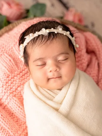 A beautiful, happy smile from a newborn nestled in a basket of soft pink blankets and flowers.