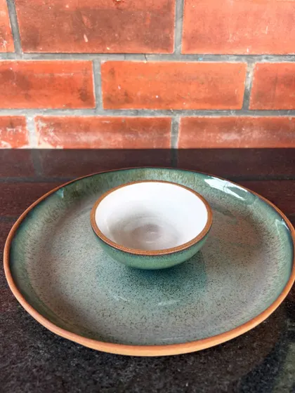 A simple and elegant chip-and-dip plate made by a student. The form was thrown on the wheel, showcasing a clean design and a lovely green speckled glaze.