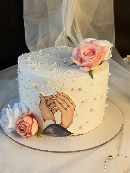 A simple yet elegant cake for a 25th wedding anniversary. The design features an edible image of the couple's hands, symbolizing their enduring love, surrounded by delicate pearls and silk flowers.
