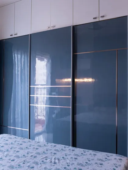 A sleek bedroom wardrobe with glossy blue sliding doors and delicate rose gold inlays. The reflective surface makes the room feel larger and adds a touch of modern elegance.