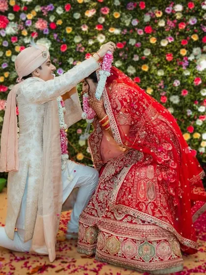 Another angle of the Varmala ceremony, showing the groom kneeling as the bride garlands him, with flower petals showering down.