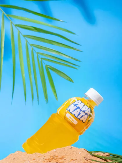 A bright, summery shot of a Papa Nata lemon drink on a mini beach setup. The vibrant blue and yellow colors make the product pop, perfect for a refreshing beverage brand.