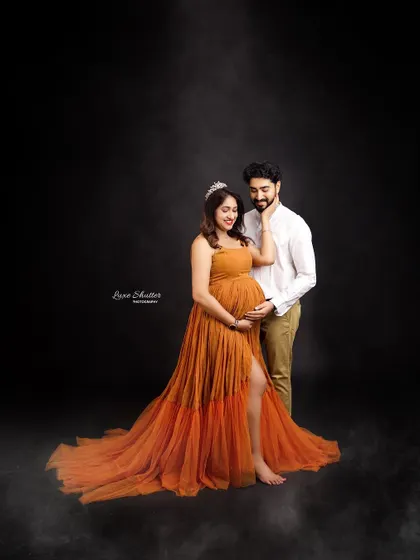 A stunning maternity portrait with a touch of drama. The flowing orange gown and smoky effects create a powerful and artistic image against a dark studio background.