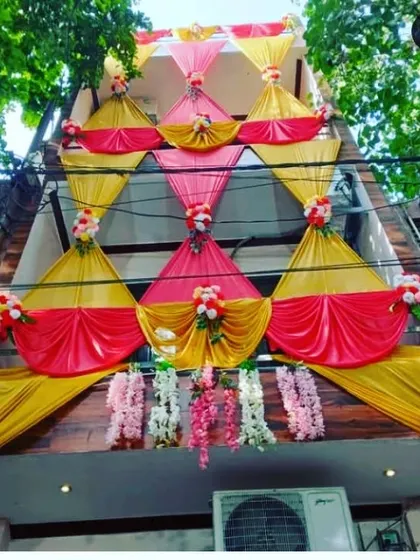 An elaborate house facade decoration with a multi-layered design of pink and yellow drapes and floral accents.
