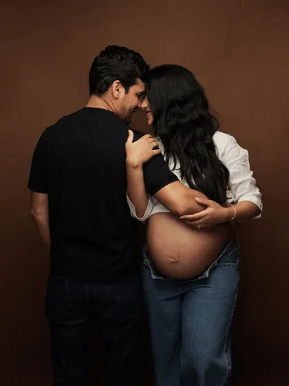 An intimate and loving pose from a studio maternity session, where the couple's connection is the central focus against a warm, brown backdrop.