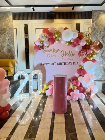 "Goodbye Teens, Hello Twenties!" A chic setup for a 20th birthday, featuring a custom backdrop and a pink, red, and gold balloon arch.