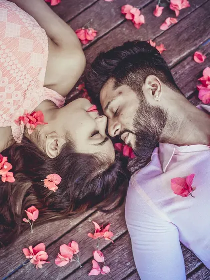 An overhead shot of a couple lying on a wooden deck, surrounded by scattered pink flower petals. This artistic composition creates a soft and romantic pre-wedding portrait.