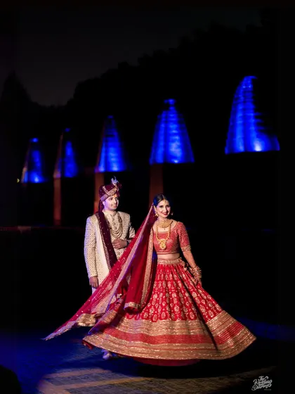 A stunning night portrait of the couple. The bride's red lehenga pops against the dark background and cool blue lights, creating a visually striking image.