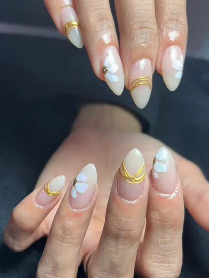 A beautiful set of almond-shaped nails with a milky white base, accented with gold lines and subtle white heart details.