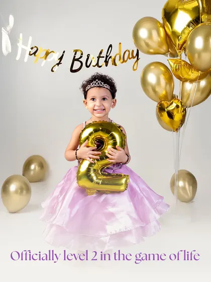 Officially level 2 in the game of life! Holding a golden '2' balloon and wearing a tiara, this little princess is the star of her second birthday photoshoot.
