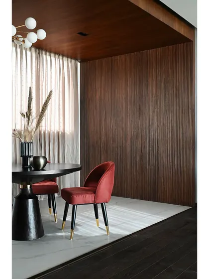 A detail shot of a private meeting nook within the Chairman's office. The rich texture of the fluted wood wall contrasts beautifully with the bold red velvet of the chair, showcasing a focus on material and color.
