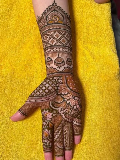 A close-up of a hand with a traditional Indian mehndi design, featuring bells and checkerboard patterns.