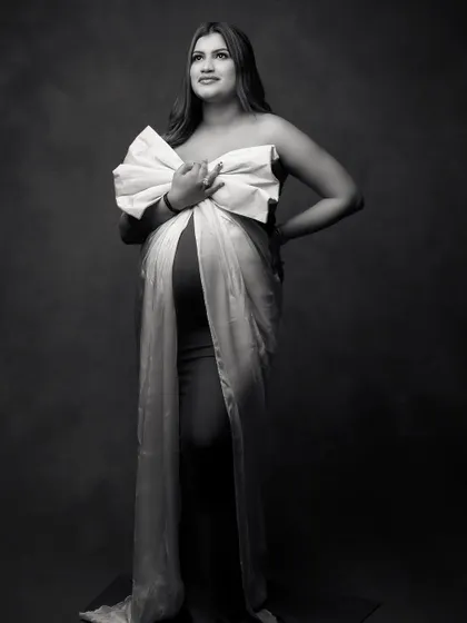 A full-length black and white portrait showcasing the elegant silhouette of the expecting mother. The contrast emphasizes the beautiful shape of the baby bump and the dramatic bow.