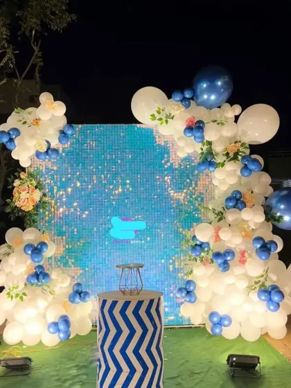 An outdoor party with a shimmering blue sequin wall. The decoration features a white and blue balloon garland, creating a beautiful photo backdrop.