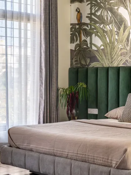 This bedroom embodies the essence of a tropical forest, with a striking wallpaper that serves as a naturalistic mural. The deep green velvet headboard and ample natural light create a space that feels connected to nature.