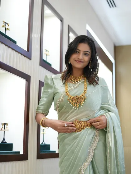 Sonu trying on a traditional gold vaddanam (waist belt) over the saree, completing the look.