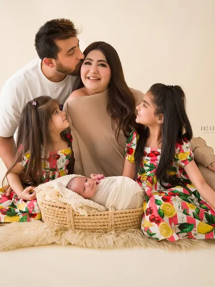 A portrait of adoration. The whole family gathers around the newborn, with older sisters looking on with love and wonder.