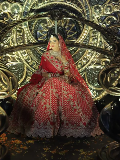 A regal pose from a bride in a red lehenga. She is seated on a throne-like chair, looking every bit the queen on her wedding day.
