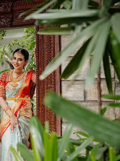 A bride, framed by lush green leaves, looks out from an antique doorway, a beautiful and natural portrait.