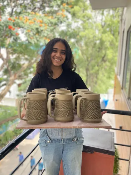 Vrinda proudly holding a tray of her hand-carved beer mugs, part of her graduation collection.