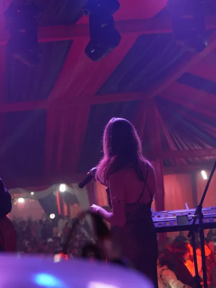 I'm seen from behind at the microphone, looking out at the audience gathered beneath the canopy for live music.