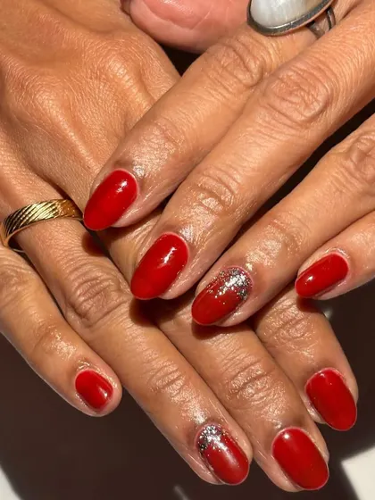 Simple, bold, and festive. This manicure features a classic glossy red polish with a sparkling silver glitter accent nail, proving that sometimes a timeless combination is all you need for a standout look.