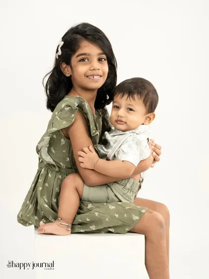 The sweet bond between siblings. An older sister holds her baby brother, both dressed in matching green outfits, sharing a gentle moment.