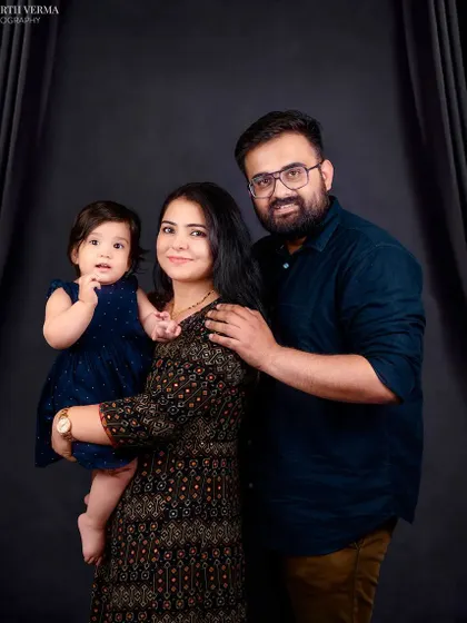 A classic family pose with the mother holding her baby and the father standing protectively beside them. A timeless portrait of a loving family.