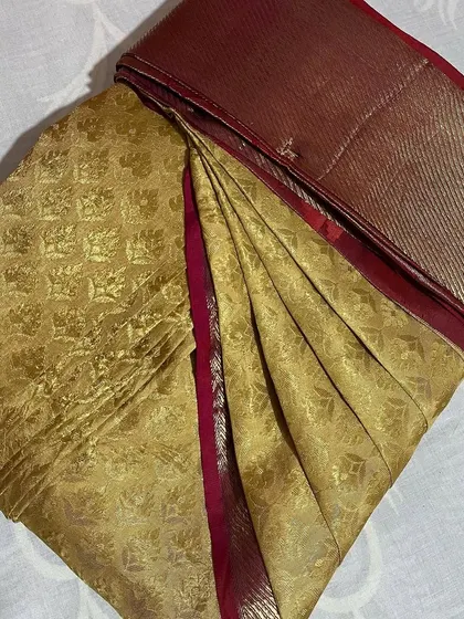 A gold tissue saree with a maroon border, ready for a party. The pleats are crisp, ensuring the saree holds its shape.