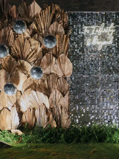 A "Starry Night" themed sangeet photo booth, with a backdrop of dried palm leaves, a sequin wall, and a neon sign.