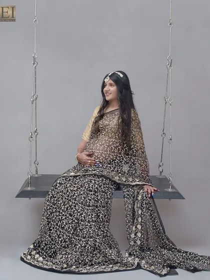 A whimsical portrait on a studio swing set, with the mom-to-be looking radiant in her black and gold saree.