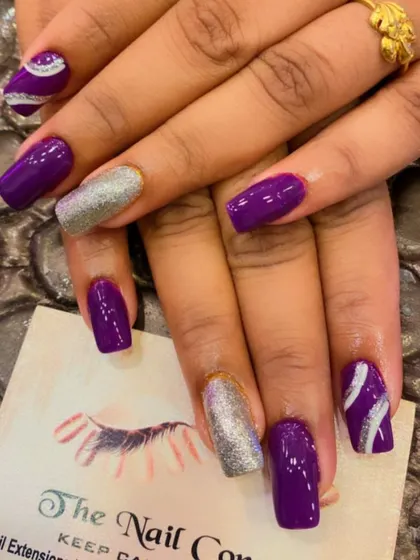 A bold and glossy set of square nails. The deep purple polish is paired with silver glitter accent nails and purple nails with a silver swirl design.