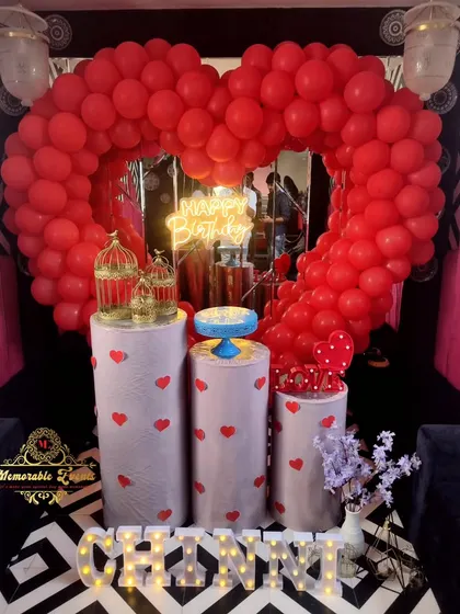 A cute birthday setup with a red heart balloon arch and plinths decorated with small red hearts.