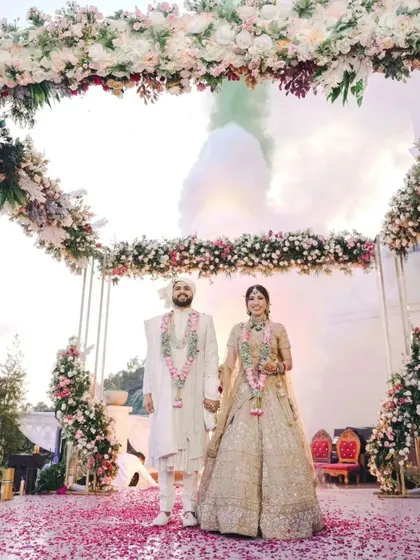 The couple's grand entrance under a magnificent floral archway. With colored smoke and a shower of petals, this photograph captures the scale and splendor of a beautifully orchestrated wedding ceremony.