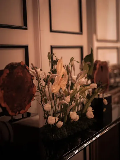 A minimalist yet striking floral arrangement featuring elegant calla lilies and white roses. Placed against a paneled wall, this detail shows our ability to create beauty in simplicity, complementing the overall luxurious theme.