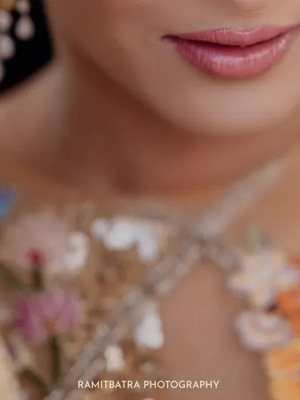 A macro shot focusing on the bride's soft smile and the intricate floral embroidery of her Rahul Mishra outfit.