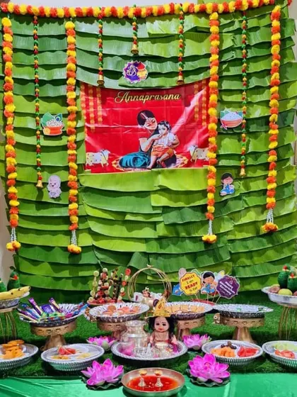 A complete setup for an Annaprasana (first rice-eating ceremony). The decor includes a themed backdrop and a full arrangement of food items and offerings on decorated plates.