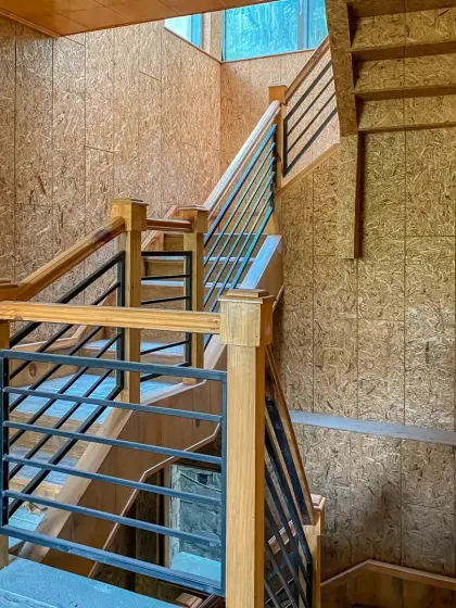 The main staircase, constructed with wood and metal railings, wraps around a central well. The walls are paneled with oriented strand board (OSB), adding a modern, textural element to the rustic design.