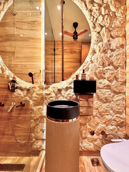 In this powder room, I combined a rough, natural stone wall with smooth, wood-paneled surfaces. The custom pedestal sink and large circular mirror create a bold, modern statement, turning a functional space into a ritualistic experience.