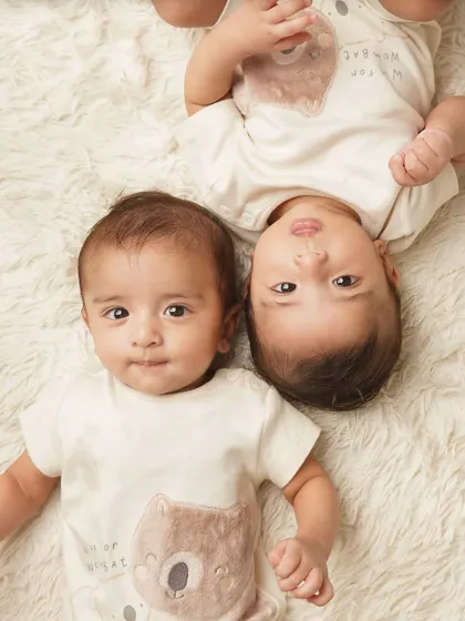 A playful shot of twin babies lying on a fluffy rug in matching bear-themed outfits. Their curious expressions are just adorable.