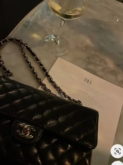A flat lay capturing the essence of quiet luxury: a classic bag, a glass of wine, and an understated elegance.