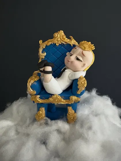 A close-up of the top-tier topper: Boss Baby relaxing in his ornate blue and gold throne, floating on a bed of fluffy clouds.