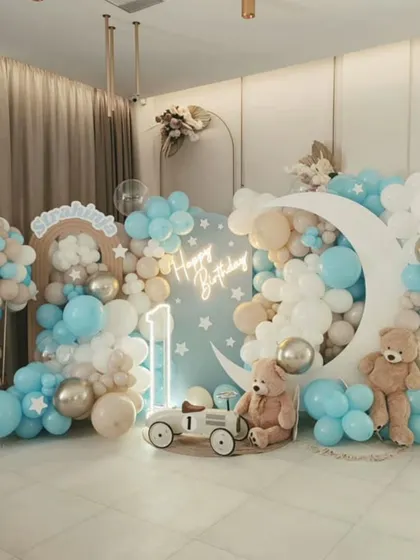 A dreamy and elegant "Twinkle Twinkle Little Star" birthday theme. This setup uses a soft blue and neutral color palette, with a large crescent moon prop, teddy bears floating on clouds, and a "Happy Birthday" neon sign to create a serene and magical photo backdrop.