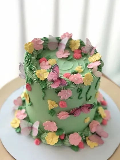 A garden-themed cake with a variety of hand-piped flowers and edible butterflies on a lovely green buttercream base.
