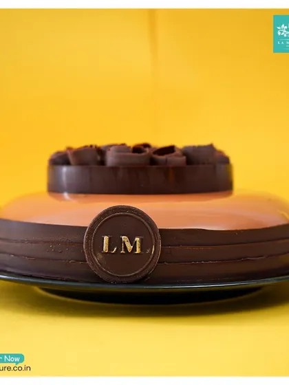 A side profile of the chocolate rose and mirror glaze cake, showing its clean lines and the impressive height of the central chocolate decoration.