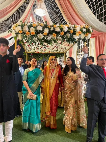 A beautiful Kashmiri bride making her entrance under a phoolon ki chaadar. The canopy is elegantly decorated with white and peach flowers, held by her loved ones.
