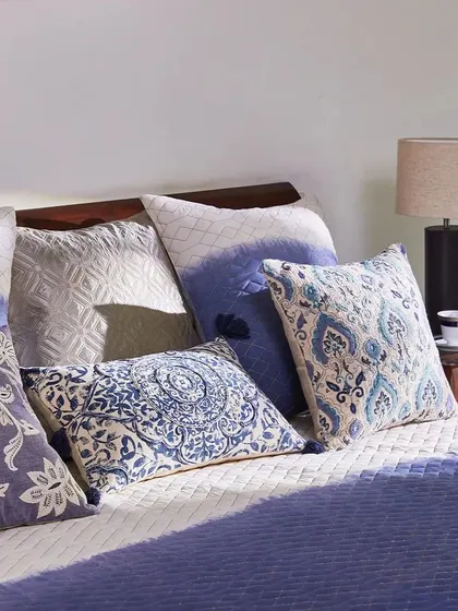Let your decor dreams take flight with my Indigo Collection. This beautifully styled bed, bathed in sunlight, showcases a variety of blue and white cushions, creating a peaceful and inviting retreat.