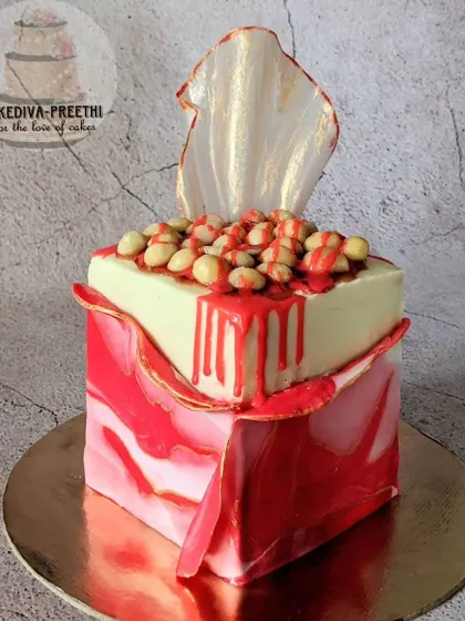A modern, artistic cake featuring a marbled red fondant wrap, a delicate rice paper sail, and a topping of macadamia nuts. This piece combines multiple textures and advanced techniques.