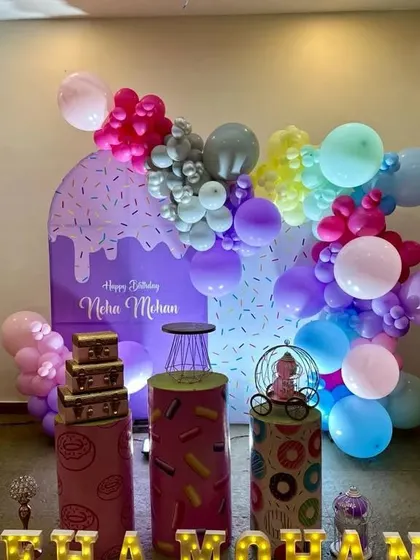 A fun and colorful donut and sweet treats themed party, with a sprinkle-covered backdrop and a rainbow of balloons.