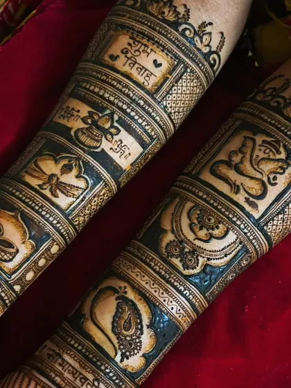 A close-up of a Maharashtrian bridal forearm design. It features auspicious symbols in separate blocks, including a kalash, diyas, a peacock, and Lord Ganesha, along with the phrase 'Shubh Vivah' (Happy Wedding).